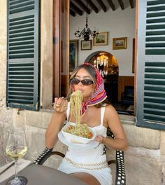 a woman sitting at an outdoor table eating food from a bowl with her hands in her mouth