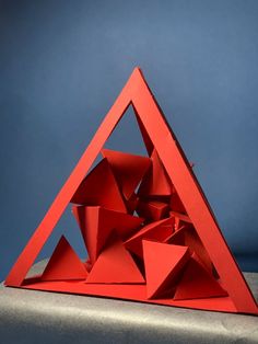 a red triangle shaped object sitting on top of a gray table next to a blue wall