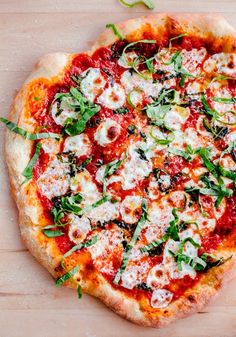 a pizza sitting on top of a wooden table covered in cheese and veggies