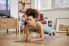 a woman is doing push ups on a yoga mat in the living room while looking at the camera