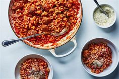 two bowls filled with pasta and sauce on top of a white counter next to silver spoons