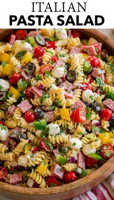 pasta salad with ham, olives, tomatoes and cheese in a wooden bowl on a striped cloth