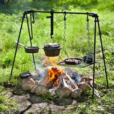 an outdoor fire pit with pots and pans on it, sitting in the grass