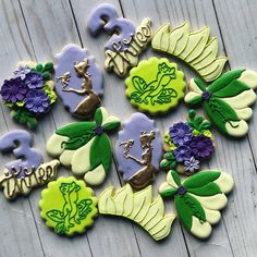 some decorated cookies sitting on top of a wooden table with purple flowers and green leaves