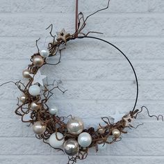 a wreath made out of branches with ornaments hanging from the top and bottom, on a white brick wall