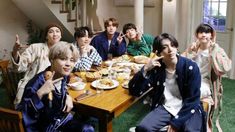 a group of young men sitting around a table eating food and giving the peace sign