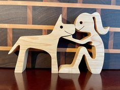 two wooden dogs standing next to each other on top of a table in front of a wall