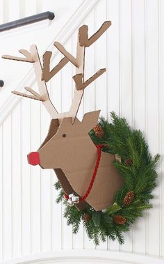 a cardboard reindeer head hanging from the side of a white wall next to a wreath