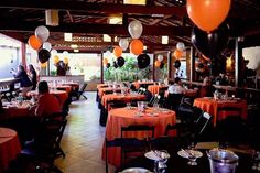 an indoor dining area with orange and black tablecloths, balloons and silverware