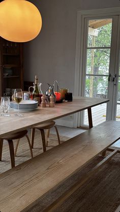 a wooden table with wine glasses and plates on it in front of a sliding glass door