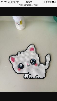 a cross stitch pattern of a white cat on a table next to a bottle of lotion