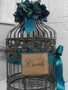 a birdcage with a sign that says cards on it and a peacock feather