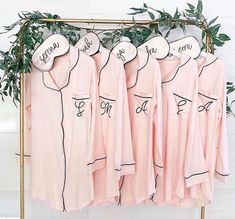 pink pajamas hanging on a rack with names written on them and green leaves in the background