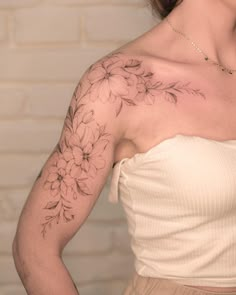 a woman with a flower tattoo on her left arm and shoulder, standing in front of a brick wall