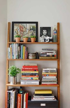 a bookshelf filled with lots of books next to a plant and pictures on the wall