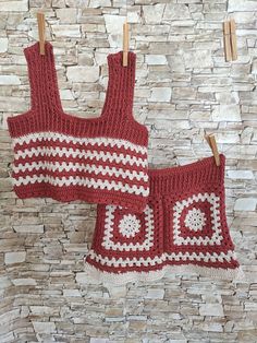 two red and white crocheted clothing hanging on clothes pins against a stone wall