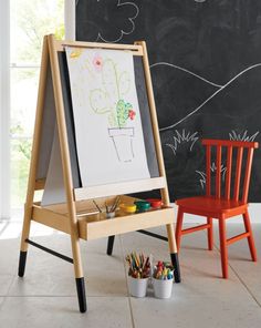 a wooden easel next to a blackboard with a drawing on it and two small children's chairs