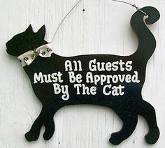 a black cat hanging on the side of a building with words all guests must be approved by the cat