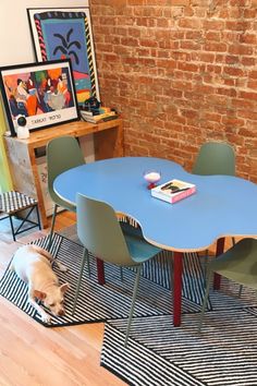 a dog laying on the floor in front of a blue table with green chairs and a red brick wall