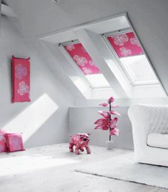 a white couch sitting under two skylights next to a pink flower vase on top of a wooden floor