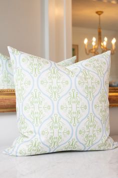 two pillows sitting on top of a white bed next to a framed mirror and chandelier