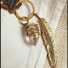 a golden keychain with a feather charm hanging from it's side on a white piece of fabric