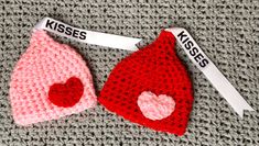 two crocheted hats with hearts on them, one is red and the other is pink