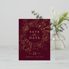 a red and gold save the date card next to a vase with flowers on it