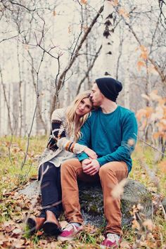 a man and woman sitting on a rock in the woods