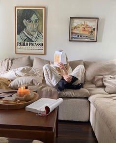 a person sitting on a couch reading a book in front of a coffee table with books