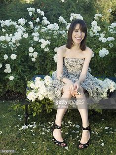 a young woman sitting on a bench in front of white flowers and greenery smiling at the camera