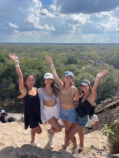 three girls standing on top of a hill with their arms in the air