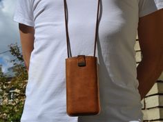 a woman wearing a white t - shirt and holding a brown leather case on her neck