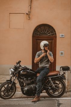 a man sitting on top of a motorcycle next to a brown building and wearing a helmet