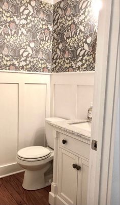 a white toilet sitting in a bathroom next to a wall papered with floral designs