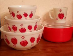 red and white bowls with strawberries on them are sitting next to a red pot