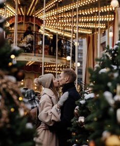 a man and woman kissing in front of a merry - go - round christmas tree