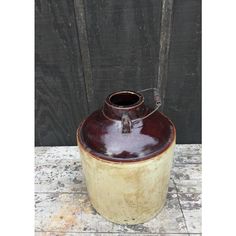 a brown and white vase sitting on top of a cement floor next to a wooden fence