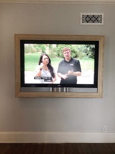 a man and woman standing in front of a flat screen tv that is mounted on the wall