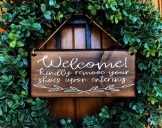 a welcome sign hanging from the side of a wooden door with greenery around it