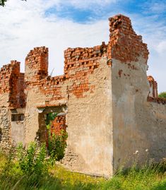 an old brick building sitting on top of a lush green field under a blue sky