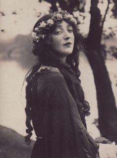 an old black and white photo of a woman with flowers in her hair standing next to trees