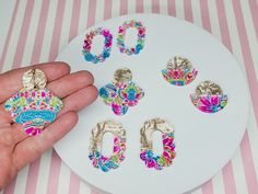 a person is holding up some decorative objects on a white plate with pink and blue stripes