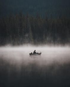 two people fishing on a boat in the foggy water