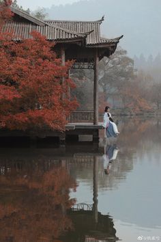 a woman holding a surfboard walking across a body of water in front of a pagoda