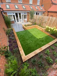 a small garden with grass and plants in the back yard, surrounded by brick buildings