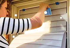 a woman is opening the shutters on her house's window with a blue sticker