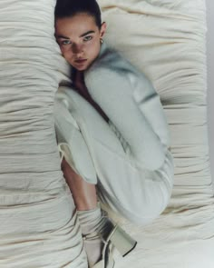 a woman laying on top of a bed covered in white sheets