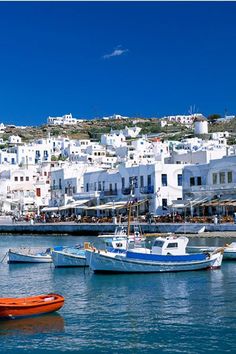 several small boats are docked in the water near white buildings and blue sky with clouds