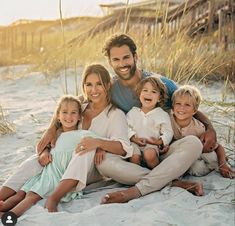 a family sitting on the beach in front of some tall grass